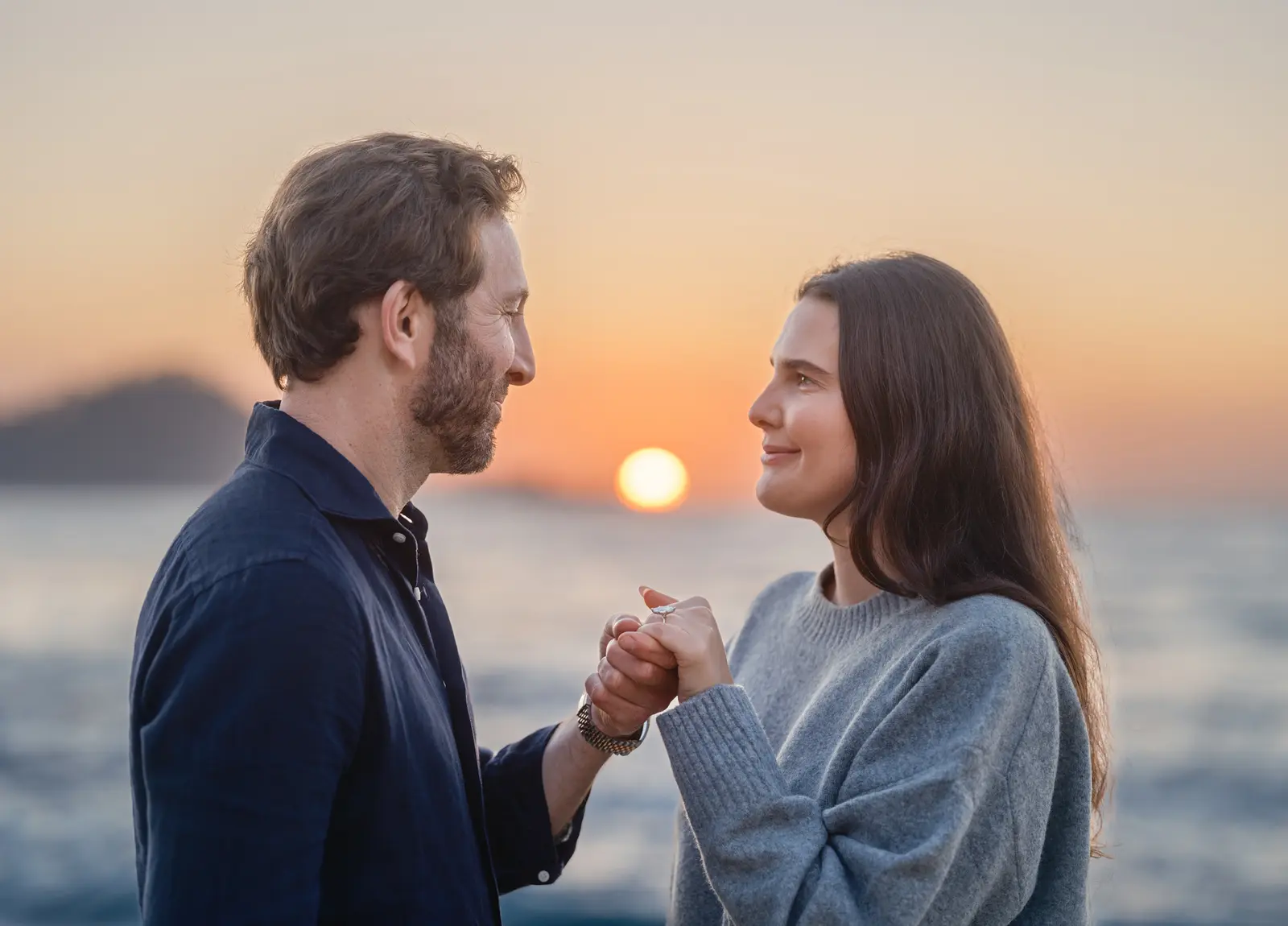Couple holding hands with new engagement ring as the sun sets over the Pacific in Carmel-by-the-Sea